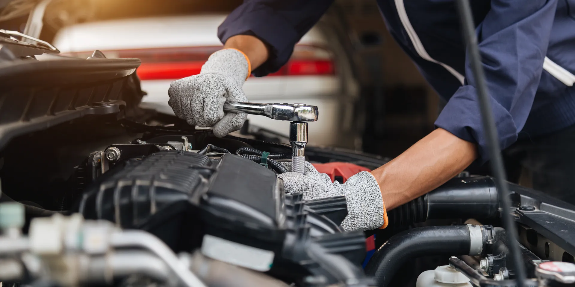 Hände in Arbeitshandschuhen setzen eine Ratsche an einem geöffneten Motorraum an