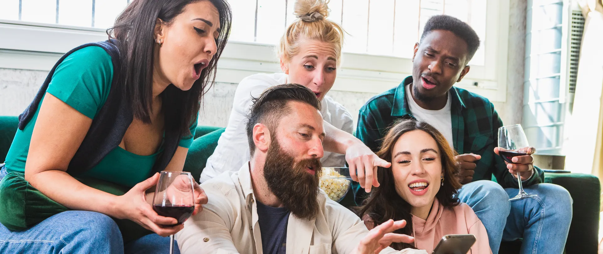 Fünf Personen drängen sich auf einem Sofa um ein Smartphone und lachen